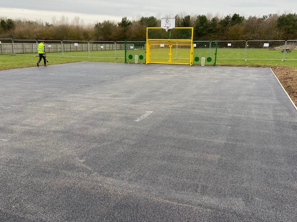 Finished tarmac base for a school multi-use games area with yellow combined goal and basketball unit in place