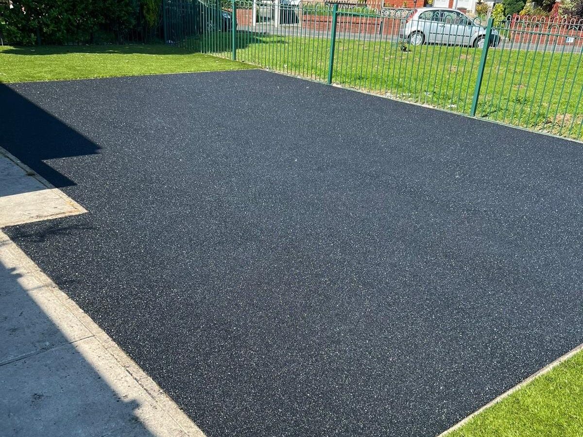 Charcoal rubber crumb surface laid as a rectangular pad, bordered by a concrete kerb, grass strip and low metal fence